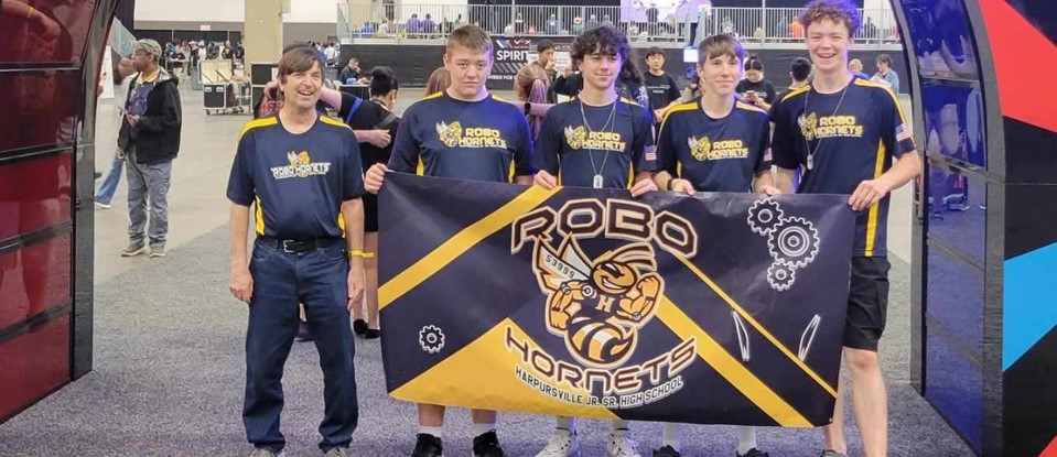 four young men and their advisor/coach holding a competition banner